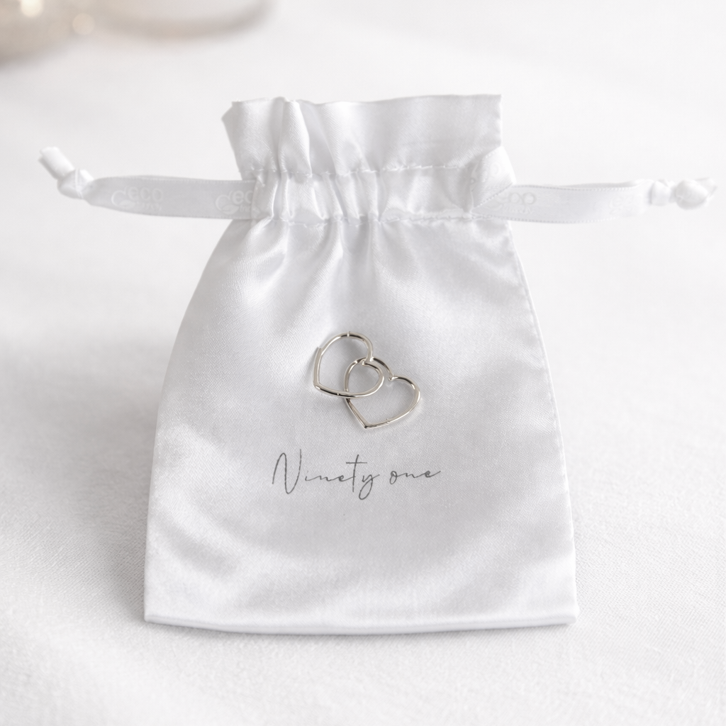 White satin drawstring bag with 'Ninety One' branding, containing two silver rings on a white background.