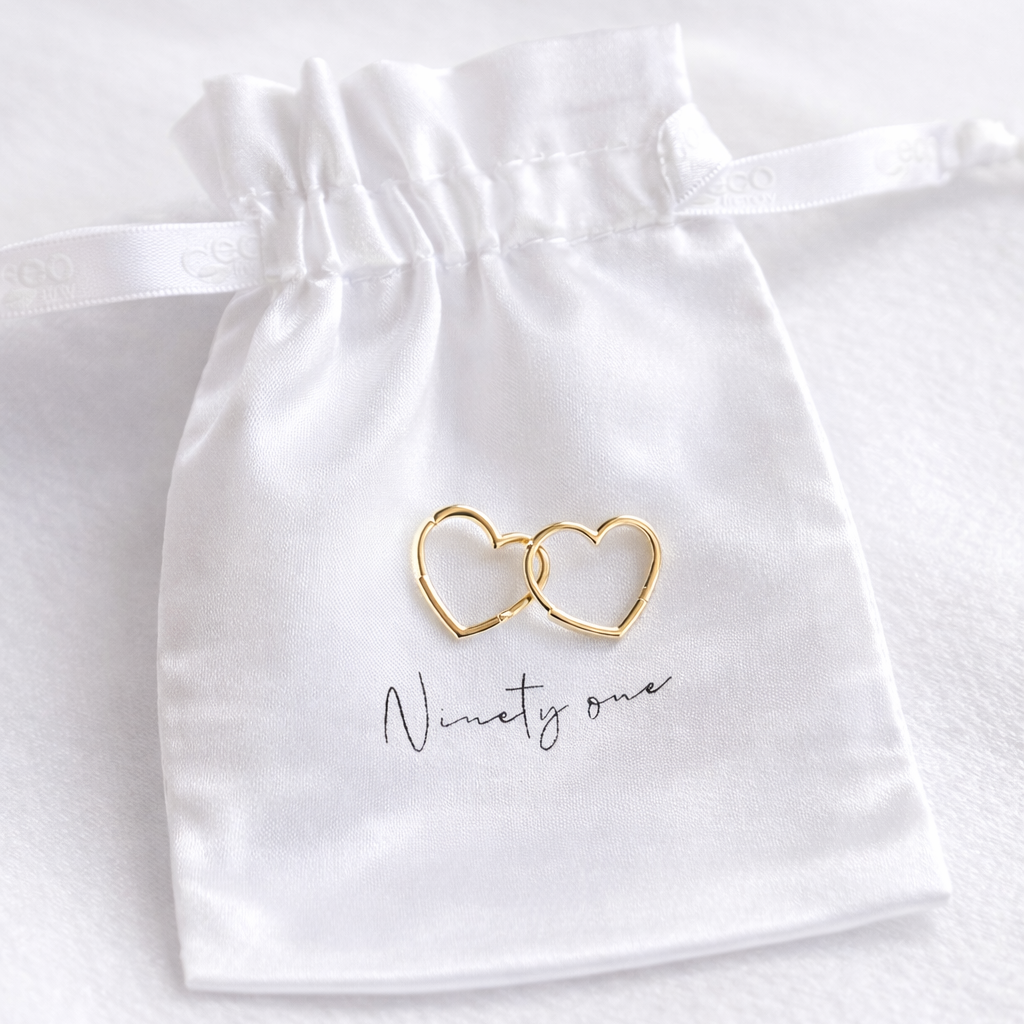 Gold double heart-shaped ring on a white satin bag with 'Ninety one' text.