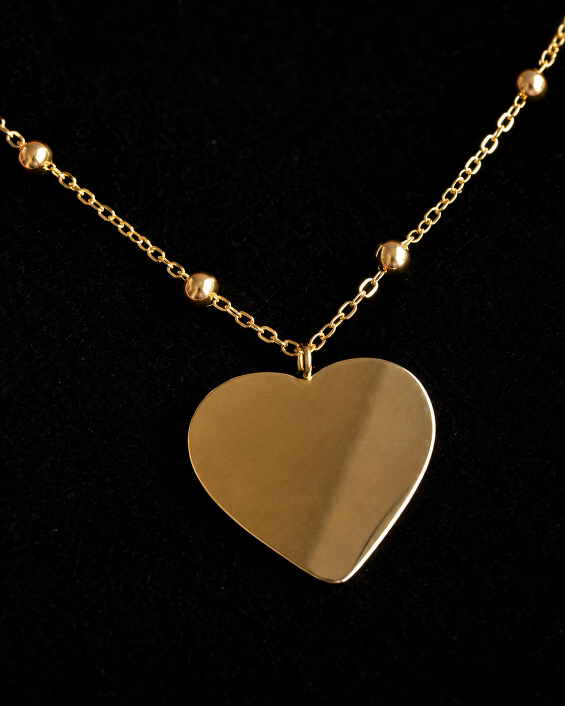 A gold heart pendant necklace with a delicate chain and small gold beads, displayed on a black background.