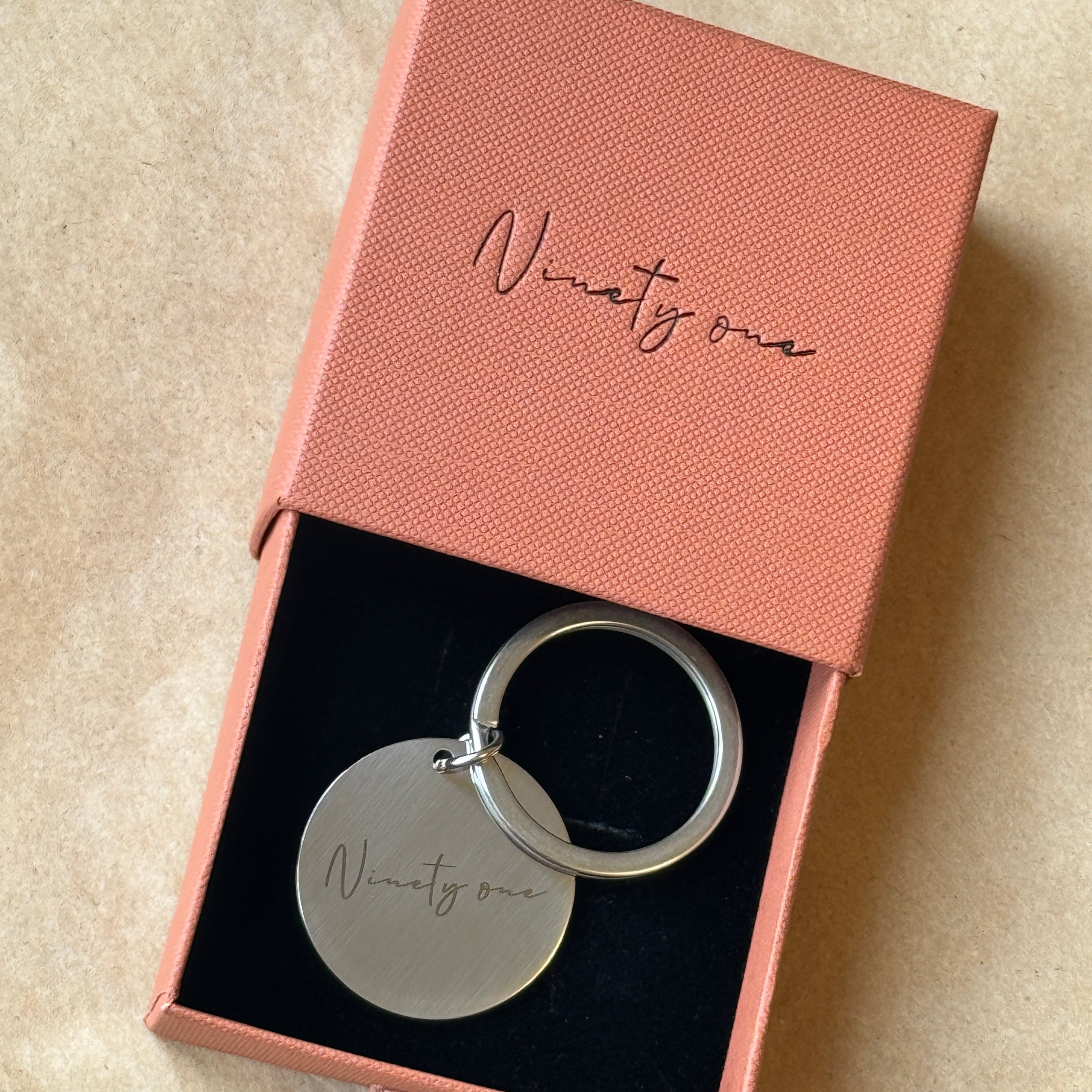 Silver keychain in a pink box with 'NinetyOne' engraved on it.
