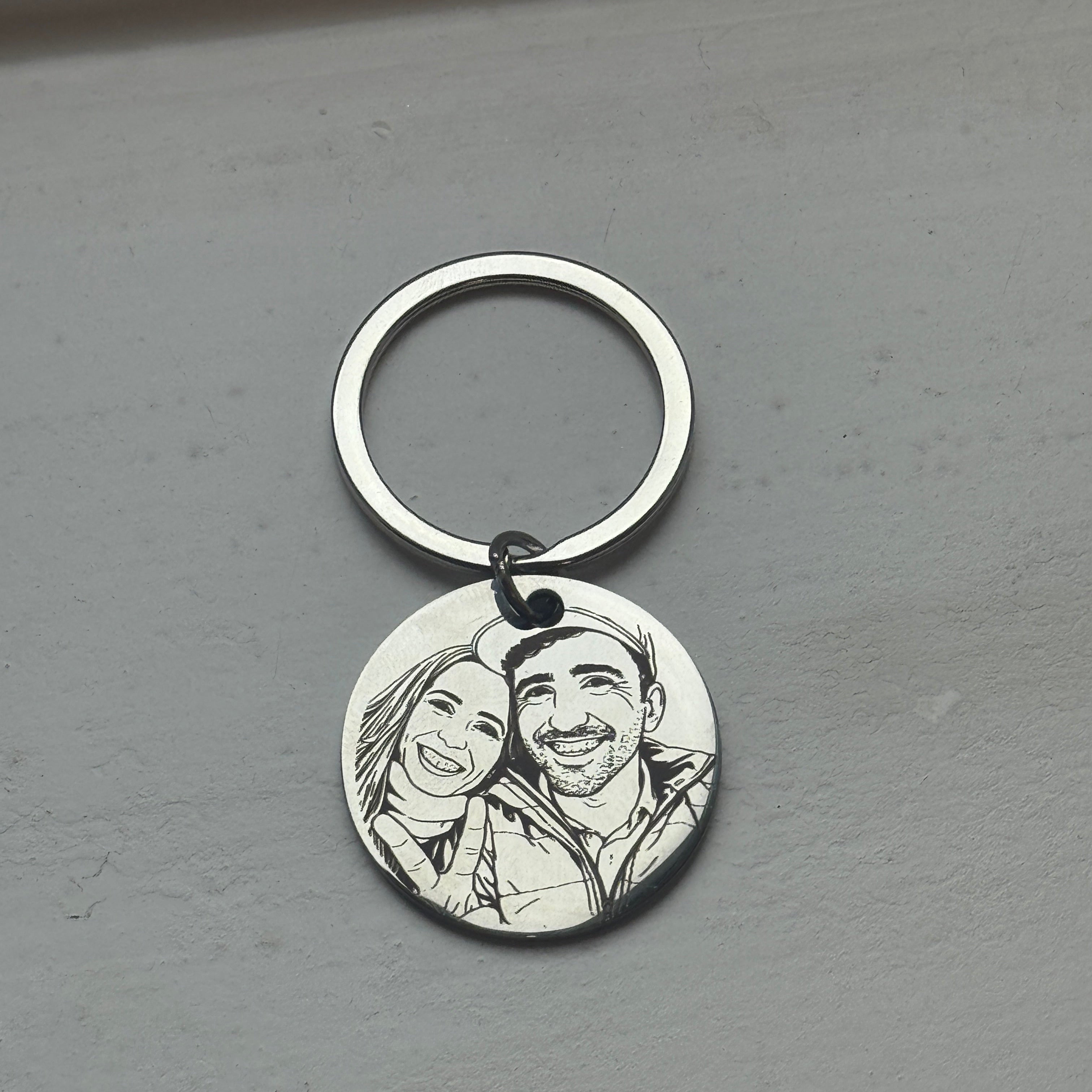 Silver keychain with engraved faces on a gray surface