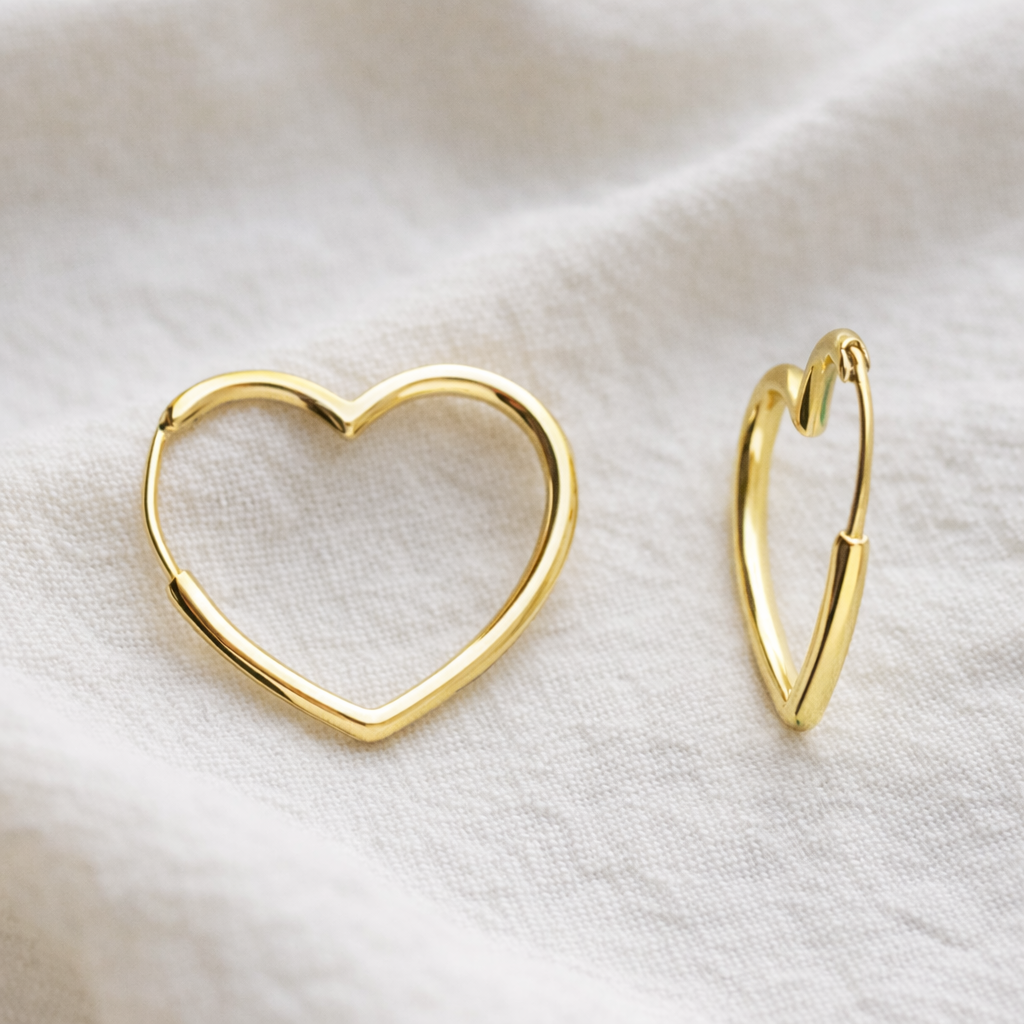 Gold heart-shaped hoop earrings on a white fabric background