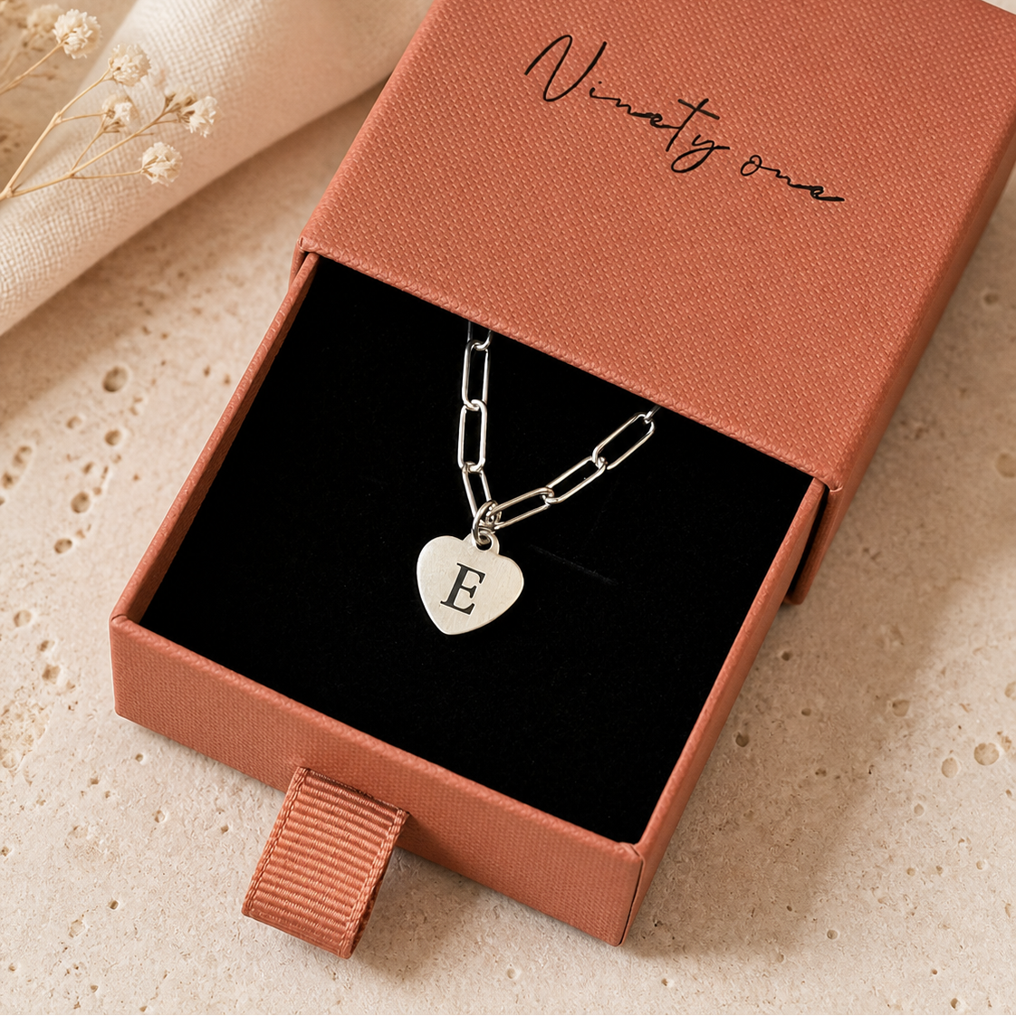 Necklace with a heart-shaped pendant and 'E' charm in an open jewelry box.
